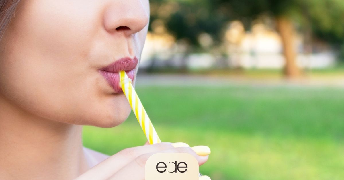 A woman using a straw to drink, demonstrating a best practice to maintain whitening results and prevent staining after consuming alcohol.