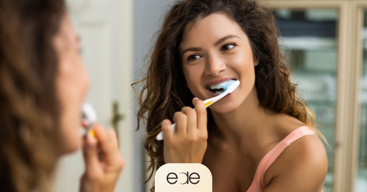 Woman gently brushing her teeth to maintain oral hygiene after dental surgery.