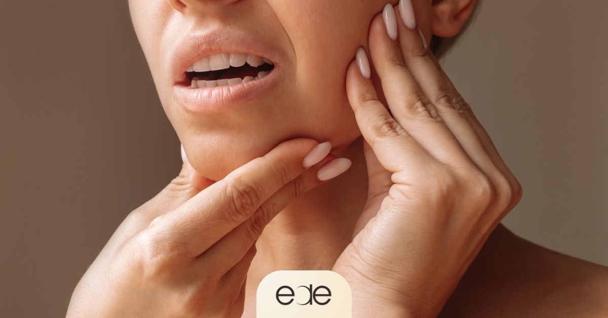 Woman touching her jaw while opening her mouth, illustrating TMJ popping or clicking.