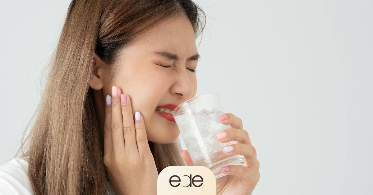 Woman experiencing tooth sensitivity while drinking cold water.